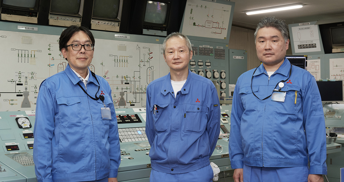 Mr. Hiroshi Aso (center), chief of the engine test team, Mr. Jun Yabana (left), H-IIA rocket project manager (PM), and Mr. Junya Takida (right), engine project engineer (PE), standing in the background of the control device used in the acceptance test ©Hibiki Watabe